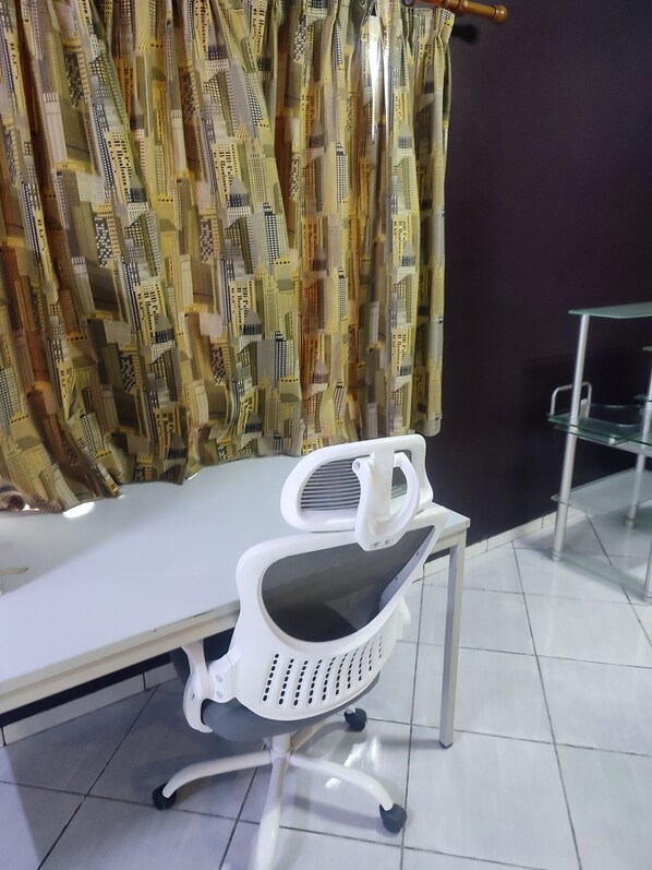 A room with a white desk, a white office chair, a glass table, and a patterned curtain.