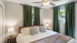 Una cama bien hecha con cabecera de madera, dos lámparas de noche y un ventilador de techo.