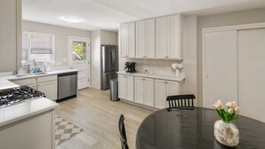 Una cocina moderna con armarios blancos, un refrigerador de acero inoxidable, una cafetera y una mesa de comedor con un florero.
