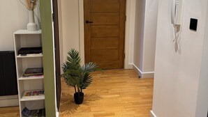 Een gang met een houten deur, een wit, aan de muur bevestigd telefoontoestel, en een kleine potplant.