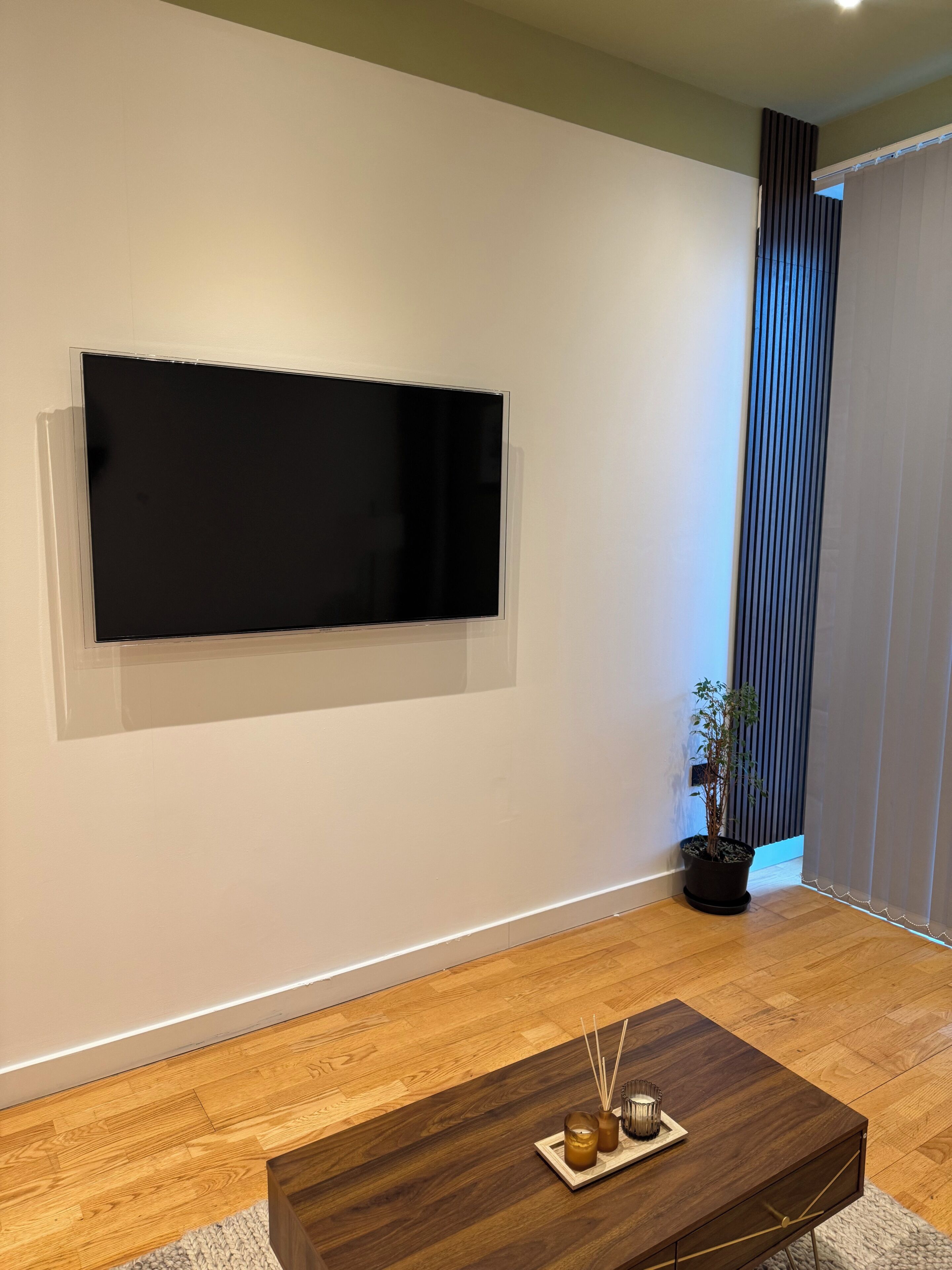 Un salon moderne avec un téléviseur à écran plat fixé au mur, une table basse en bois ornée de bougies et une plante en pot.