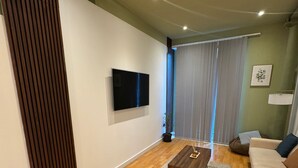 Een moderne woonkamer met een houten vloer, een flatscreen televisie aan de muur, een bank en een salontafel.