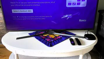 A television displaying a welcome message with a Roku logo, a remote control, and a smartphone on a white table with a decorative cloth.