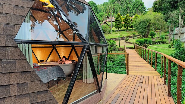 A modern glass-enclosed room with a wooden deck and a view of a lush garden. - Estalagem da Montanha (Camanducaia)