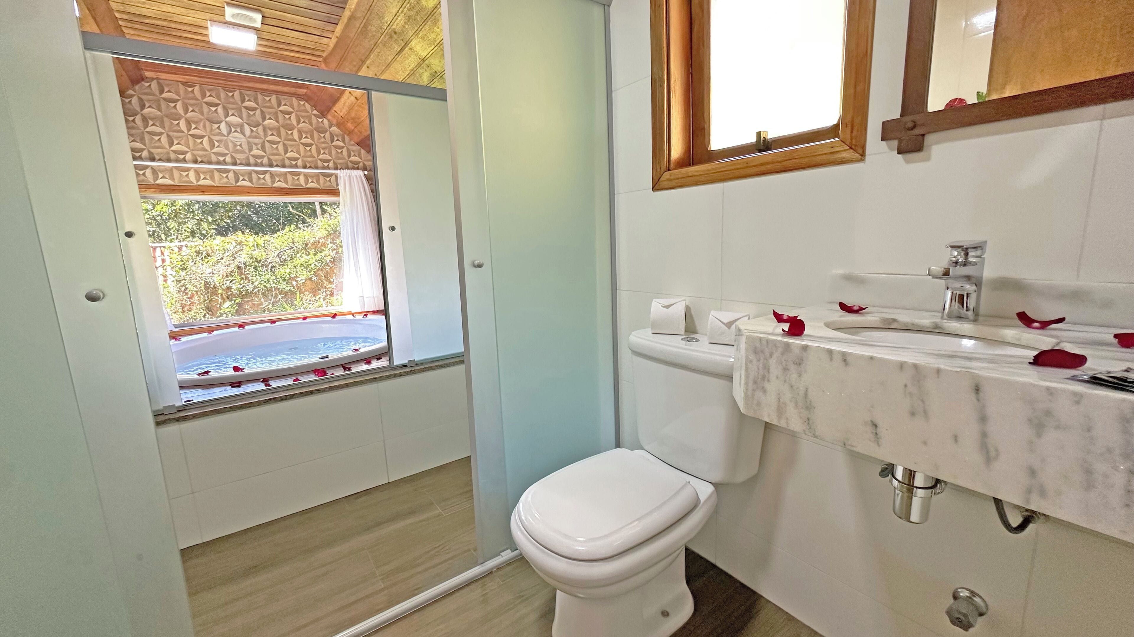 Baño con inodoro, lavabo y ventana decorada con pétalos de rosa.