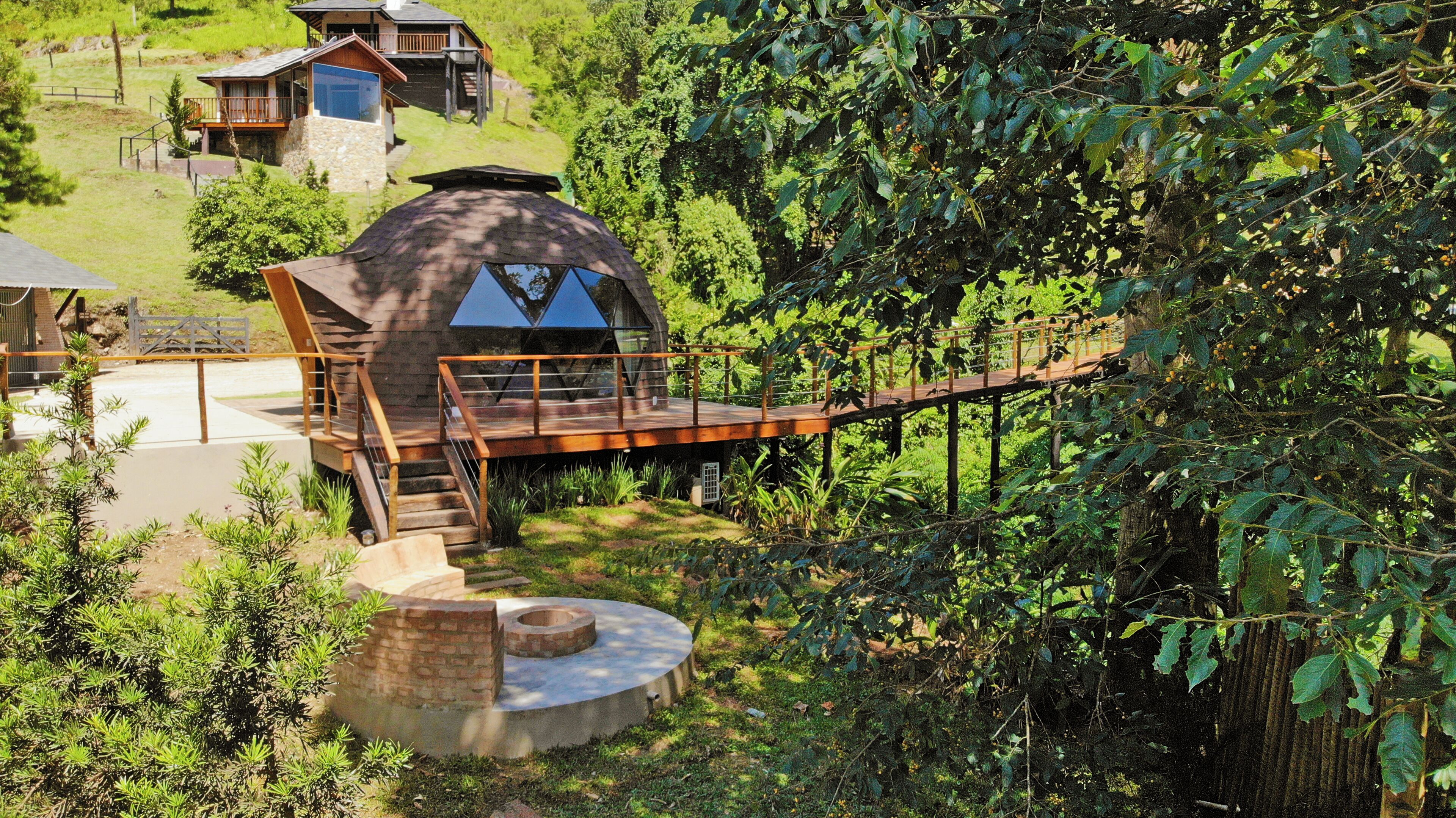 Uma casa moderna com um telhado em formato de cúpula, um deck de madeira e uma estrutura circular de pedra.