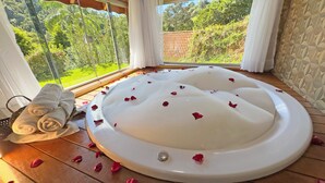 A spa room with a large bathtub, wooden flooring, and a view of greenery through large windows. - Estalagem da Montanha (Camanducaia)