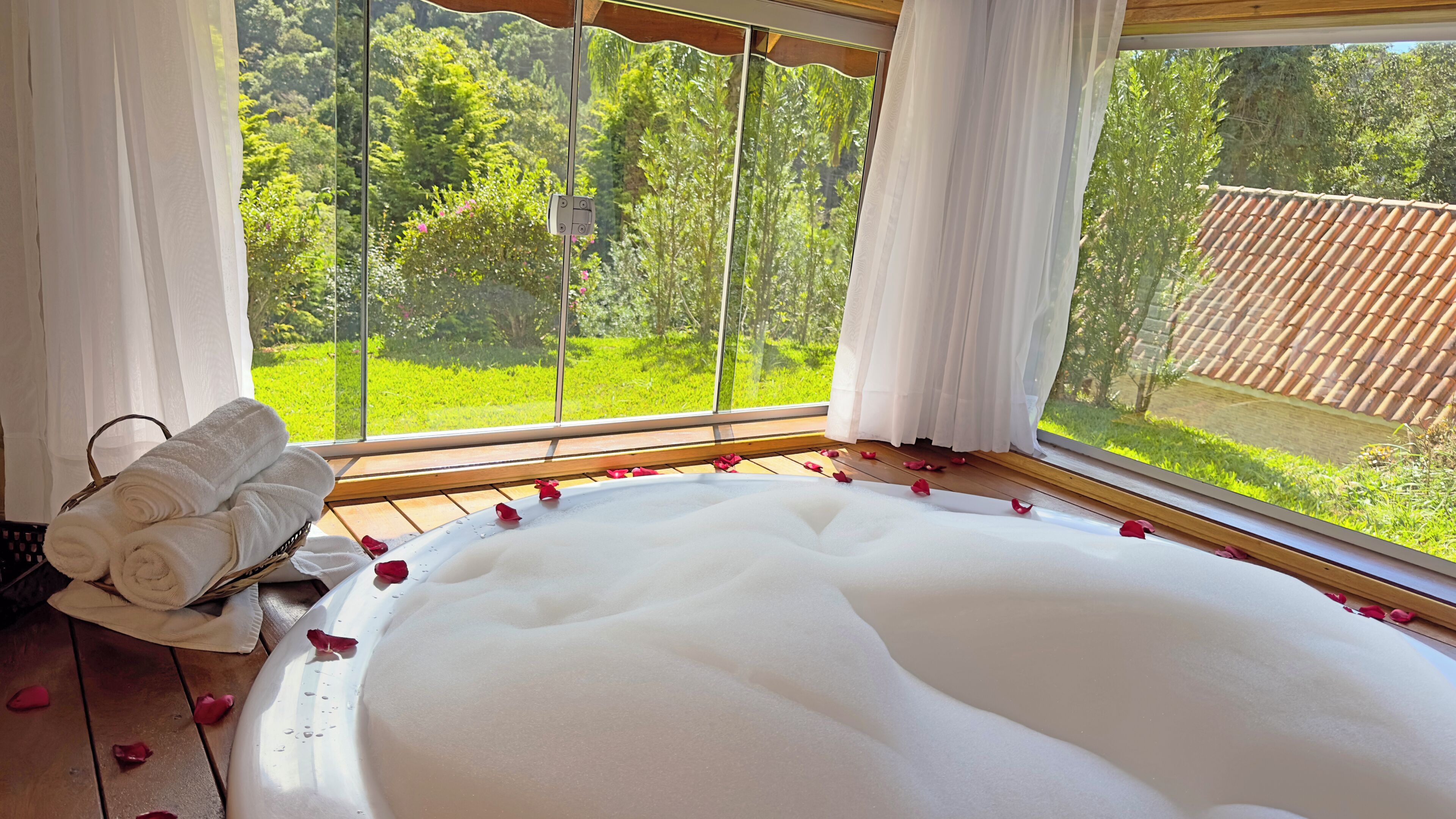 A room with a large bathtub, a wicker basket with towels, and a view of greenery outside.
