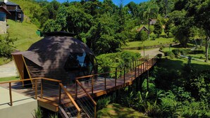 A dome-shaped building with a wooden deck leading to it, surrounded by lush greenery and hills. - Estalagem da Montanha (Camanducaia)