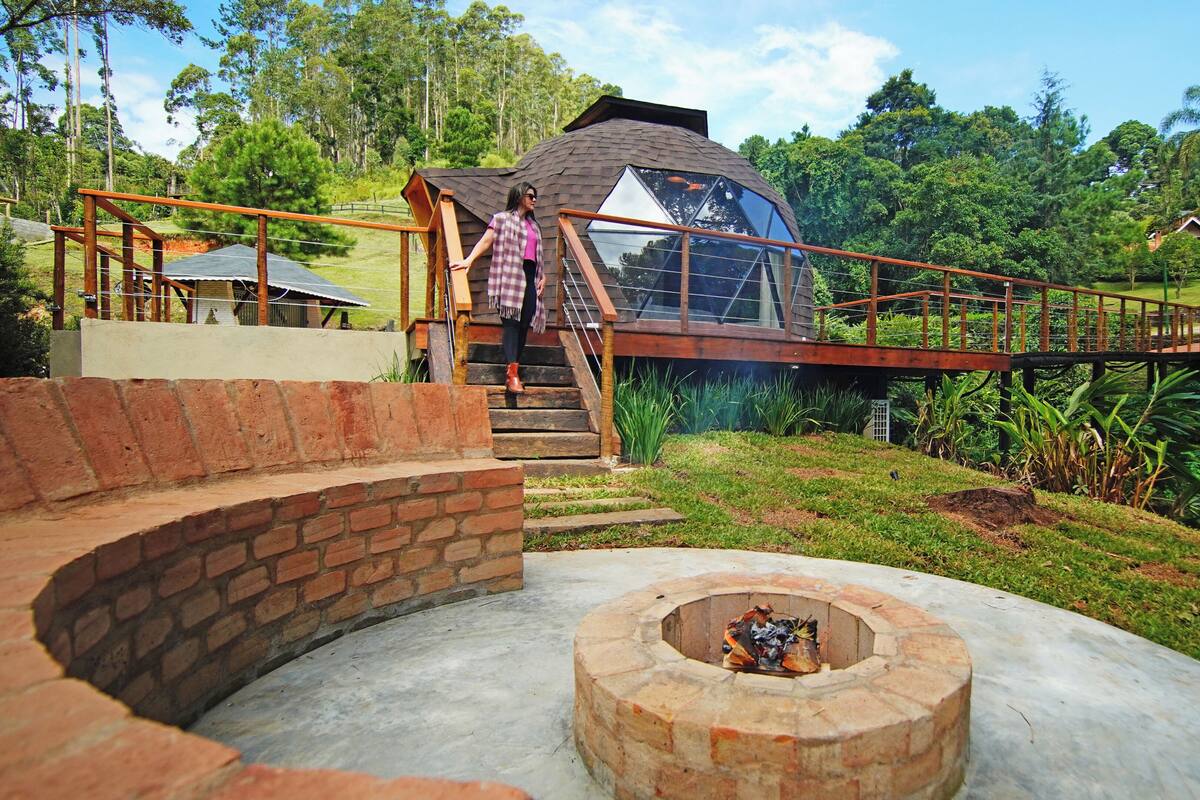 Una casa con un techo hexagonal único, una escalera de madera y un pozo de fuego circular.