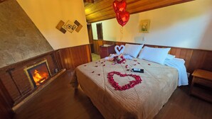 A cozy room with a fireplace, a bed with rose petals and a heart-shaped arrangement, and a red heart-shaped balloon. - Estalagem da Montanha (Camanducaia)