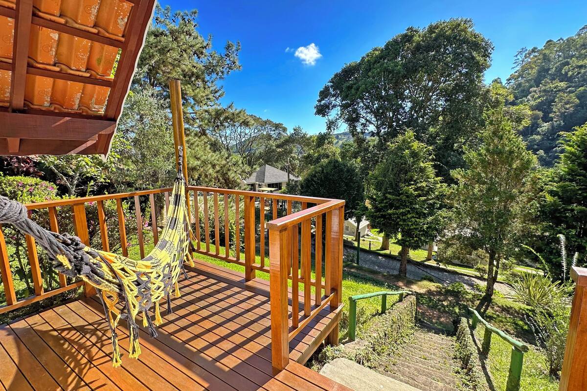 Una terraza de madera con una hamaca, barandilla de madera y vistas a una zona boscosa.