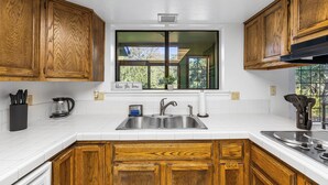 A kitchen with wooden cabinets, a double sink, and a window with a view of greenery. - Prescott Family Getaway: Spacious 4-Bedroom Retreat with Game Room and Wildlife (Prescott)