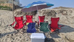 A beach with four beach chairs, a cooler, and a striped umbrella. - Nice first floor apartment (Barra Vieja)