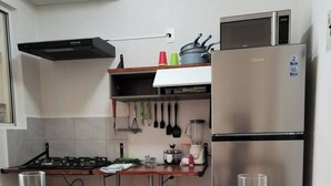 A kitchen with a gas stove, stainless steel refrigerator, and a microwave. There are two stools and a wooden table. - Nice first floor apartment (Barra Vieja)