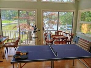 Uma mesa de pingue-pongue em um quarto com janelas amplas, um telescópio e móveis de madeira.