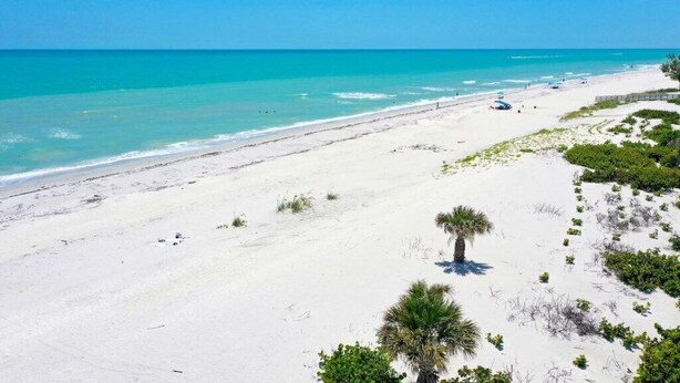 Une plage de sable blanc, avec une eau turquoise et limpide, et une végétation clairsemée.