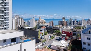 Un paysage urbain avec de hauts immeubles, un ciel bleu dégagé et une étendue d’eau visible au loin.