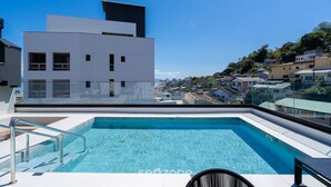 Une piscine sur le toit, avec une eau d’un bleu cristallin, entourée de bâtiments modernes et offrant une vue sur le paysage urbain en arrière-plan.