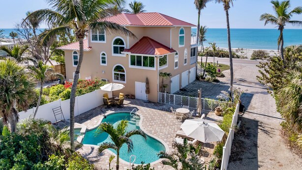 Ein zweistöckiges Haus mit Swimmingpool, umgeben von Palmen und Blick aufs Meer.