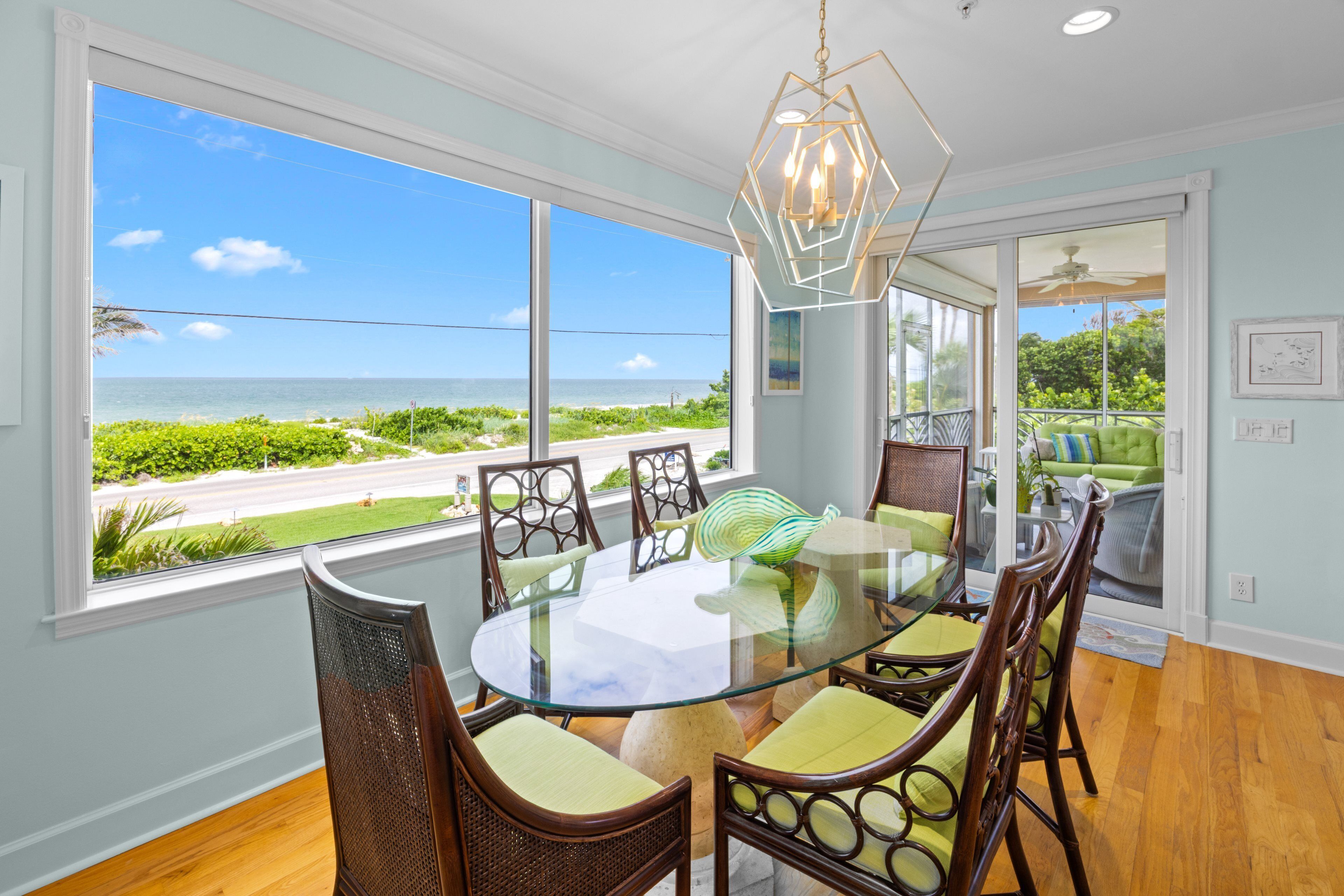 A dining area with a glass table and chairs, a view of the ocean, and a ceiling light fixture.