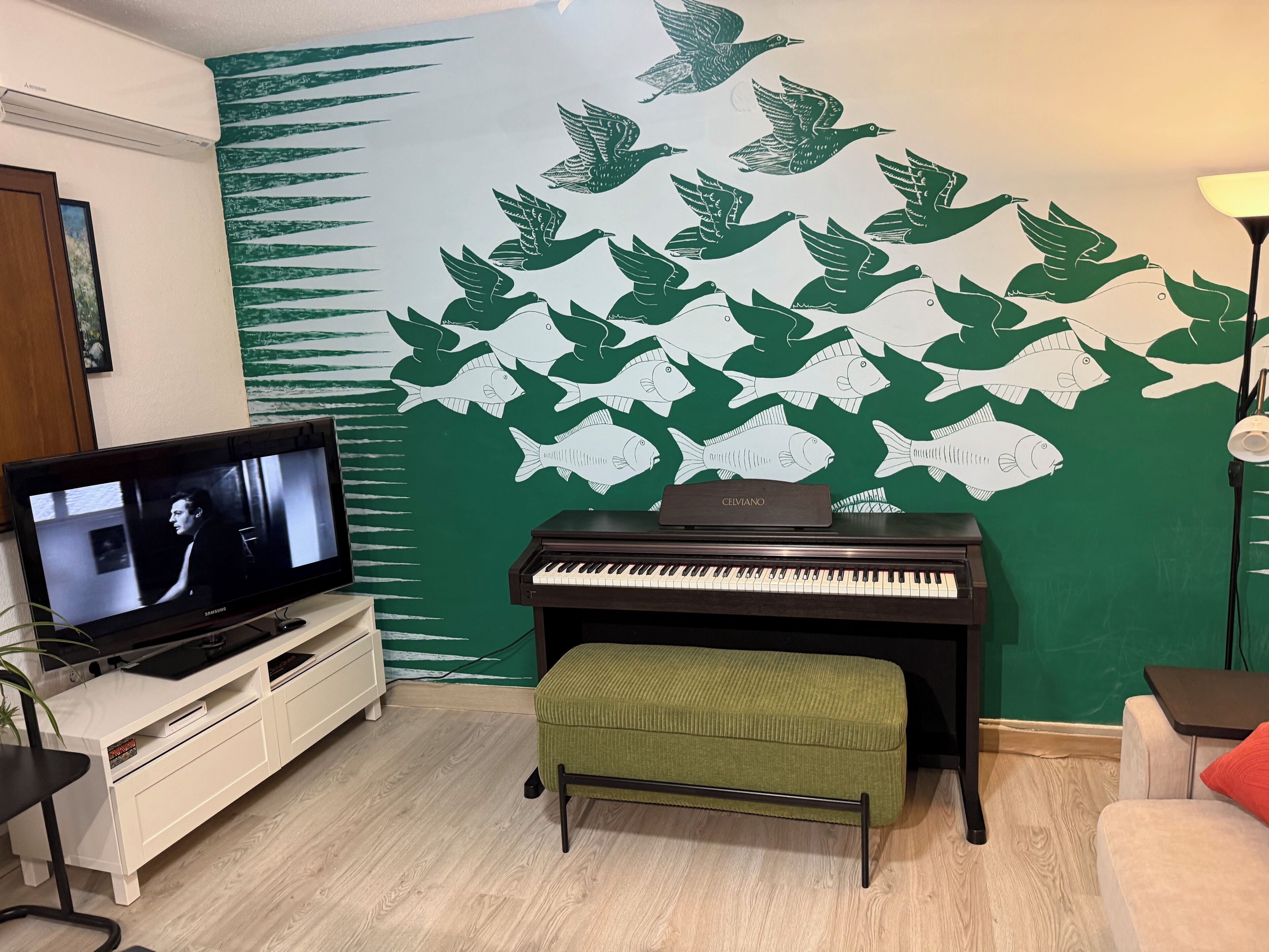 Una sala de estar con televisor, piano y un mural en la pared con pájaros y peces.