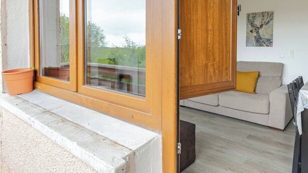 Een kamer met een schuifglazen deur naar een buitenruimte, een bank met een geel kussen, en een tafel met stoelen.