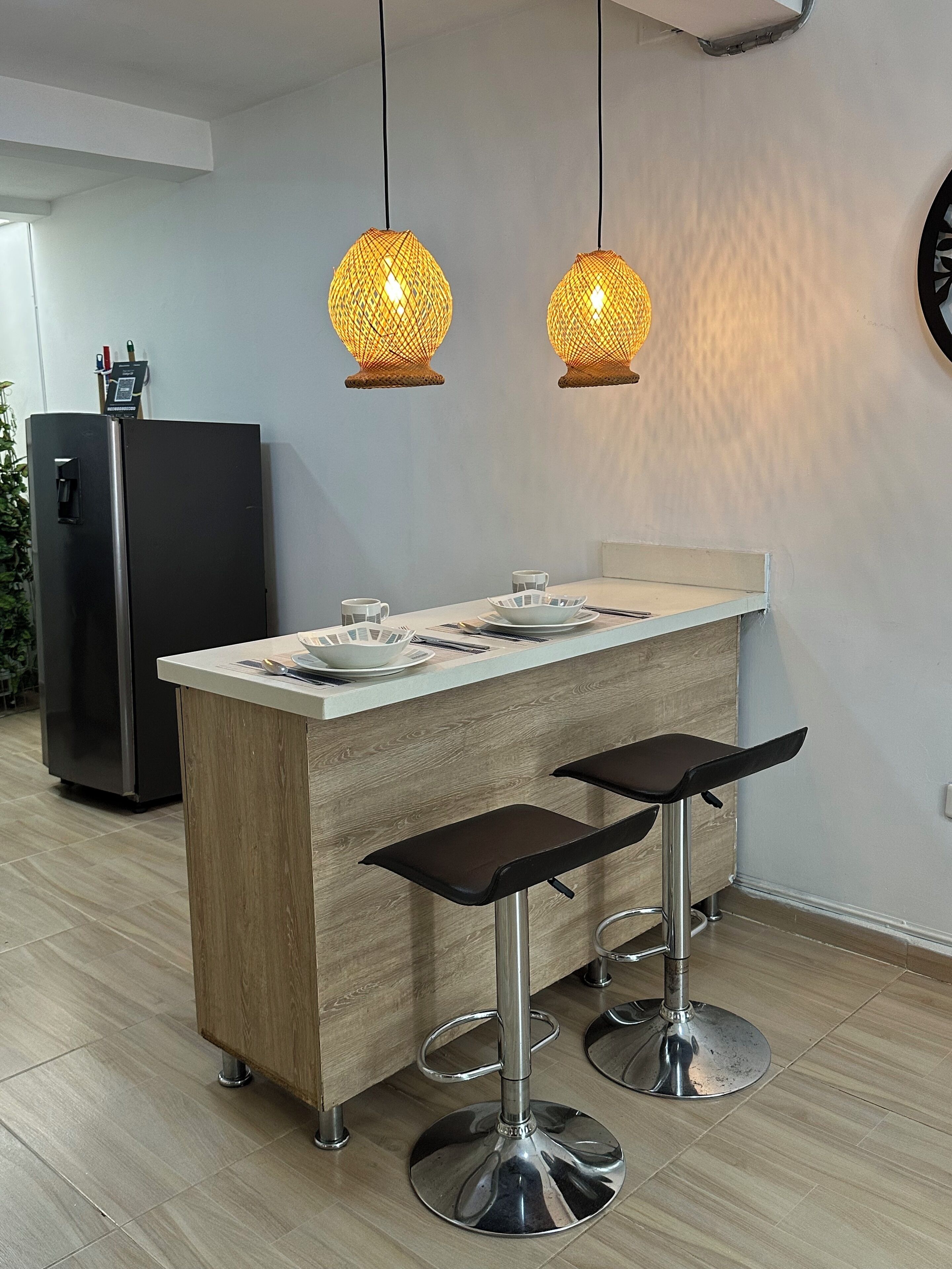 Une cuisine moderne avec un îlot central en bois, deux tabourets de bar et des luminaires suspendus.