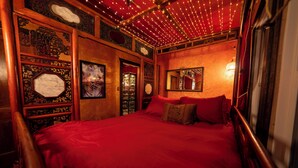 A room with a large bed, wooden headboard, and a red bedspread. There are decorative wall panels and a mirror above the bed. - Creatives Getaway in Gainesville Florida (Gainesville)