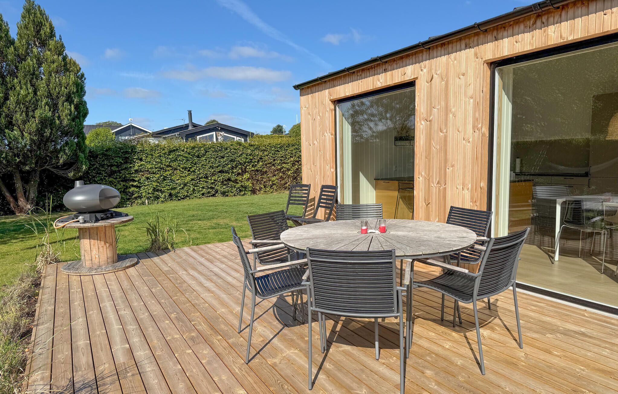 A wooden deck with a round table and chairs, a barbecue grill, and a large sliding glass door leading to an indoor area.