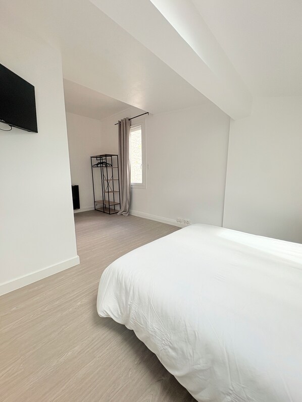 Un dormitorio con una cama grande, un armario, un televisor montado en la pared y una ventana con cortinas.