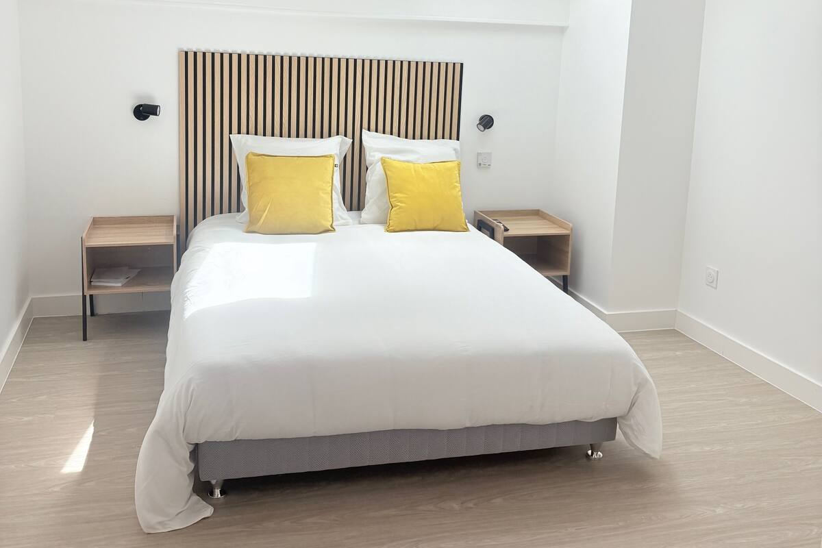 Une chambre moderne avec un grand lit, deux tables de chevet, une tête de lit à lattes et un puits de lumière.