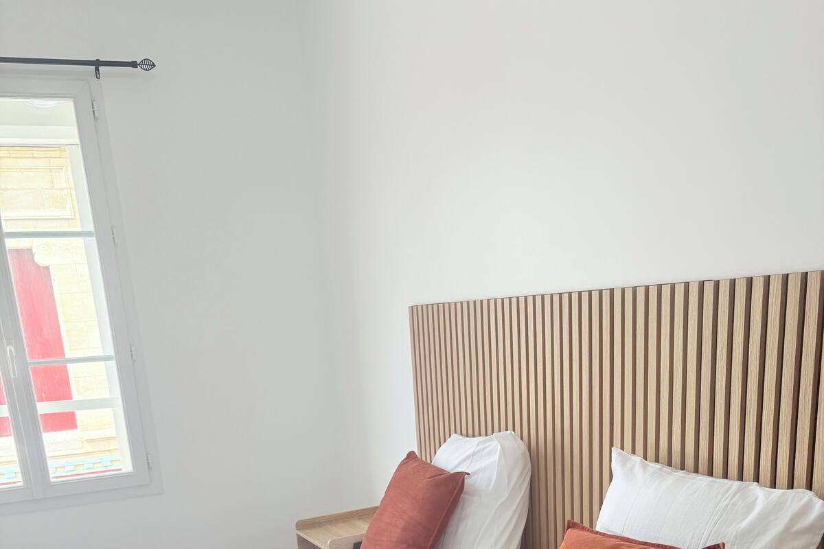 Un lit bien fait, avec une literie blanche et deux oreillers marron, une tête de lit en bois et une table de chevet avec une lampe.