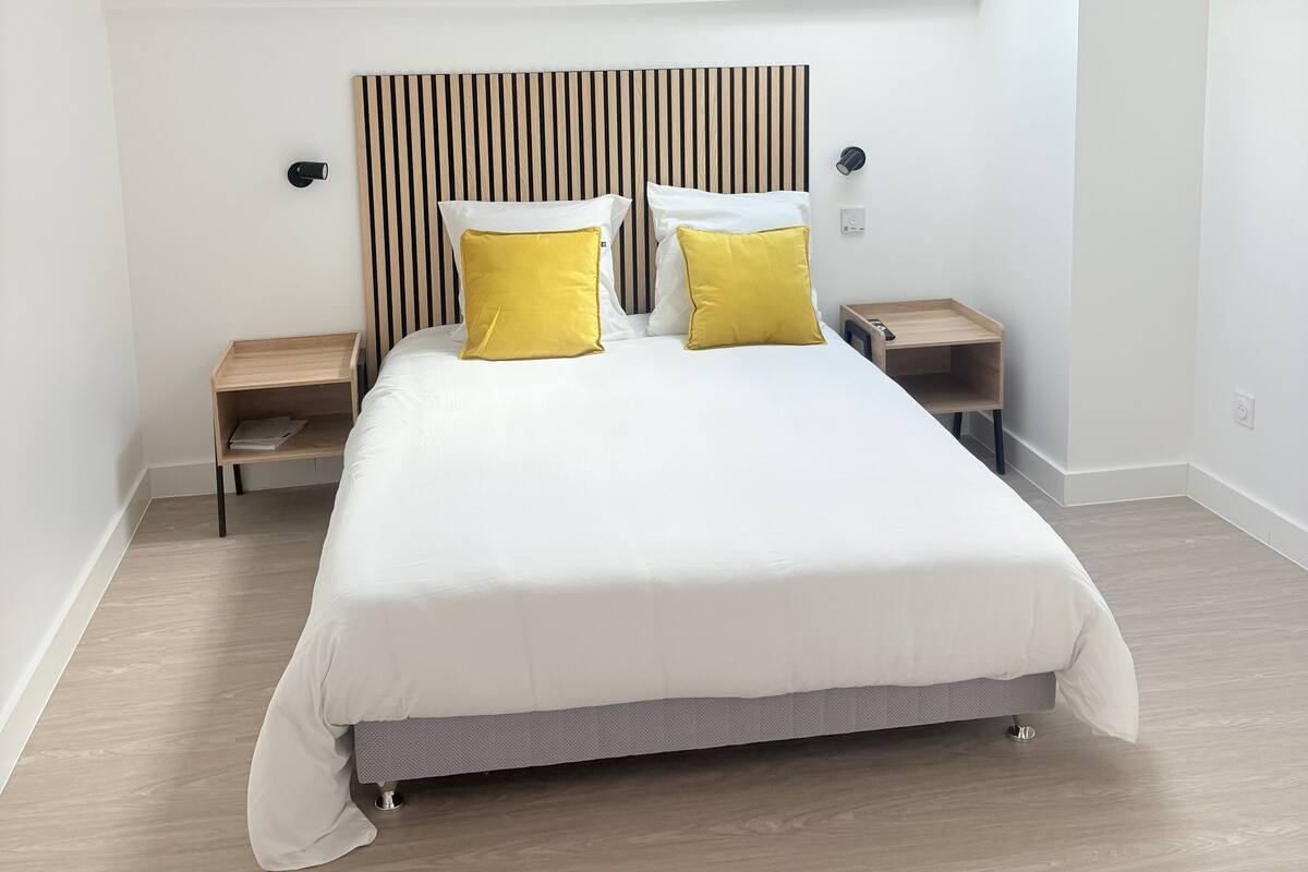 Une chambre à coucher moderne avec un grand lit, une tête de lit à lattes, deux tables de chevet et un puits de lumière.