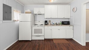 Una cocina con gabinetes blancos, un refrigerador, estufa, microondas y un reloj en la pared.