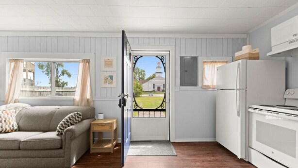 Una habitación acogedora con un sofá, una mesita, un refrigerador y una puerta que da al exterior.