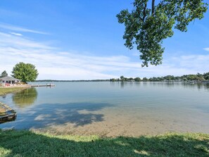 A calm lake with a dock, a grassy area, and a building with a roofed structure. - Cottage w/ Lake Access Unit 4 (Whitmore Lake)