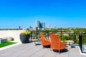A rooftop terrace with two wicker chairs, a potted plant, and a view of a city skyline. - Cozy Downtown Suite | Rooftop Lounge, Pool & Gym (Houston)