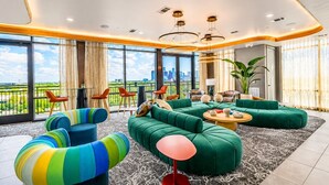 Un salon moderne avec un canapé vert, des fauteuils colorés et une vue sur le paysage urbain, visible à travers de grandes fenêtres.