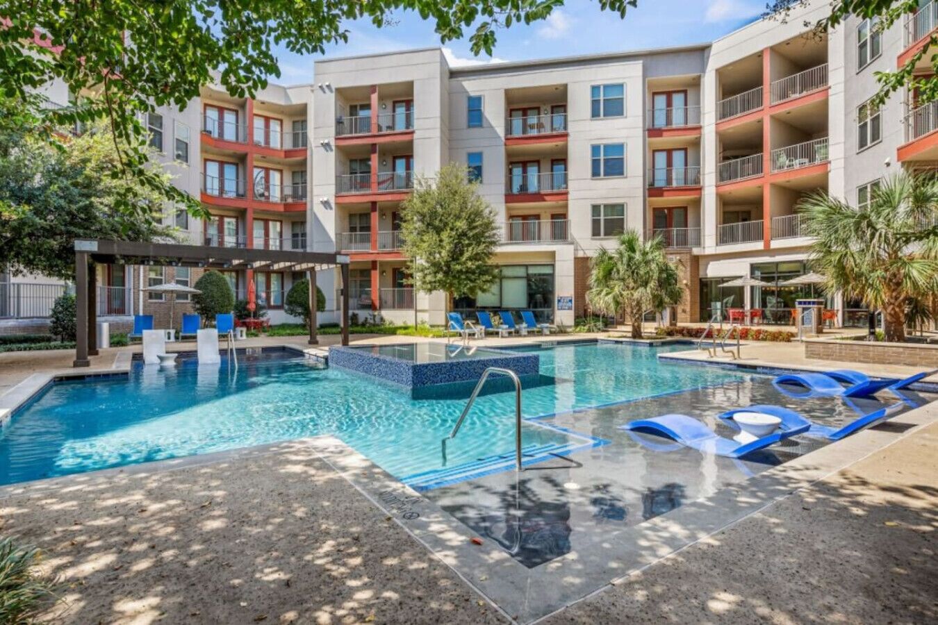 En modern lägenhetsbyggnad med en central pool, utomhusmöbler och en täckt uteplats.