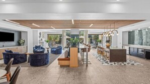 A modern living room with a large TV, blue sofas, a wooden coffee table, and a dining area with bar stools.