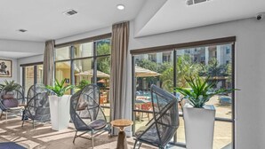 A modern hotel lobby with large windows, wicker chairs, potted plants, and a view of an outdoor pool area.