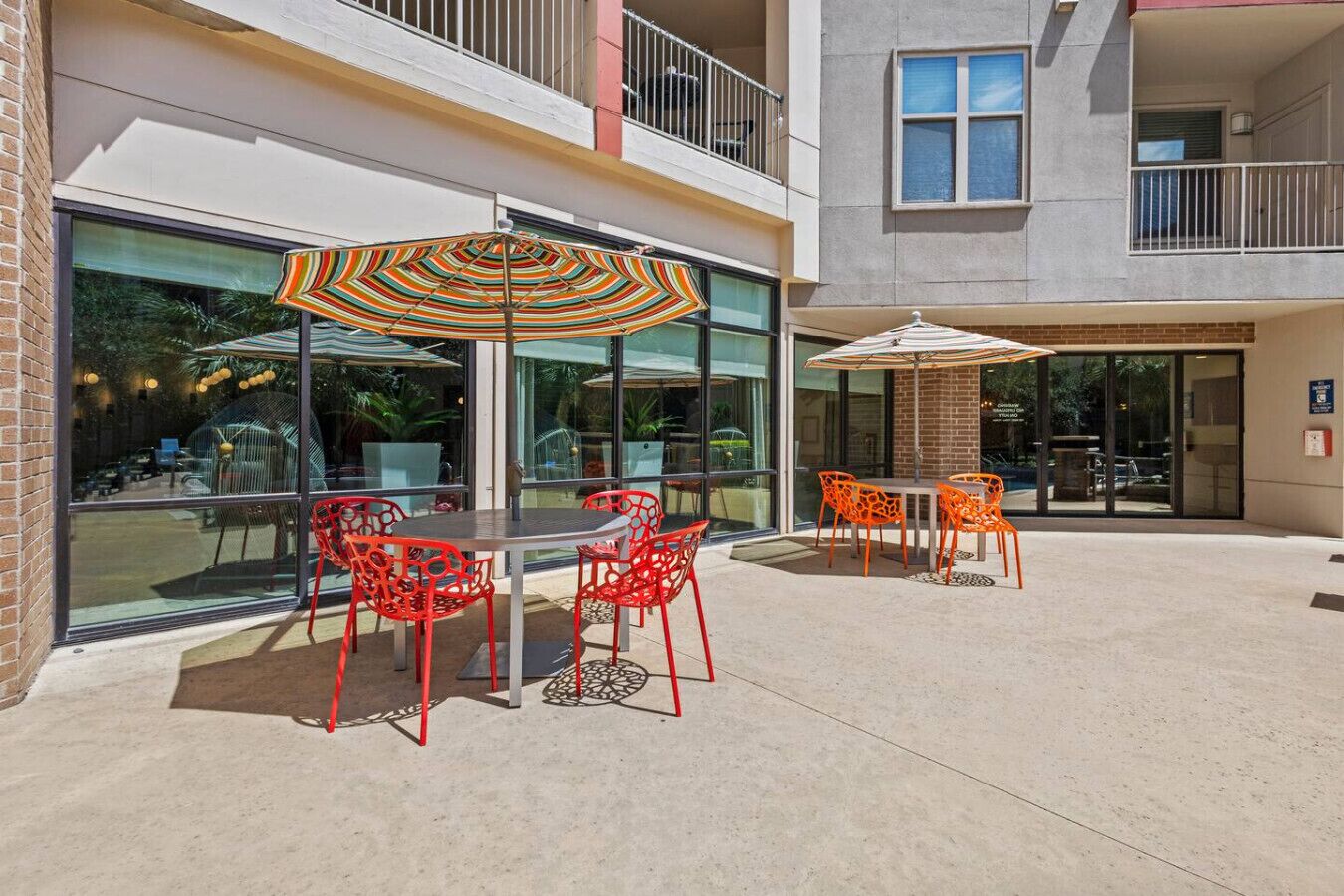 Une terrasse extérieure avec des tables et des chaises, de grandes fenêtres et un bâtiment doté d’un balcon.