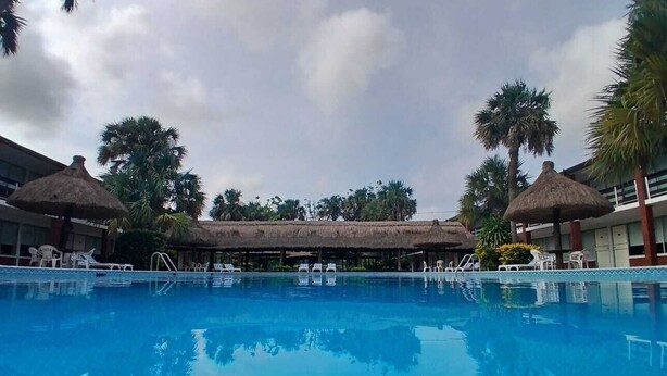 Una piscina con sillas de descanso y estructuras de techo de paja.