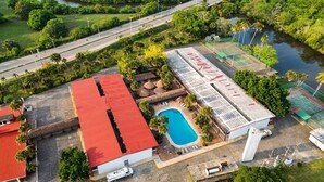 Vista aérea de una propiedad con piscina, canchas de tenis y un edificio de techo rojo.