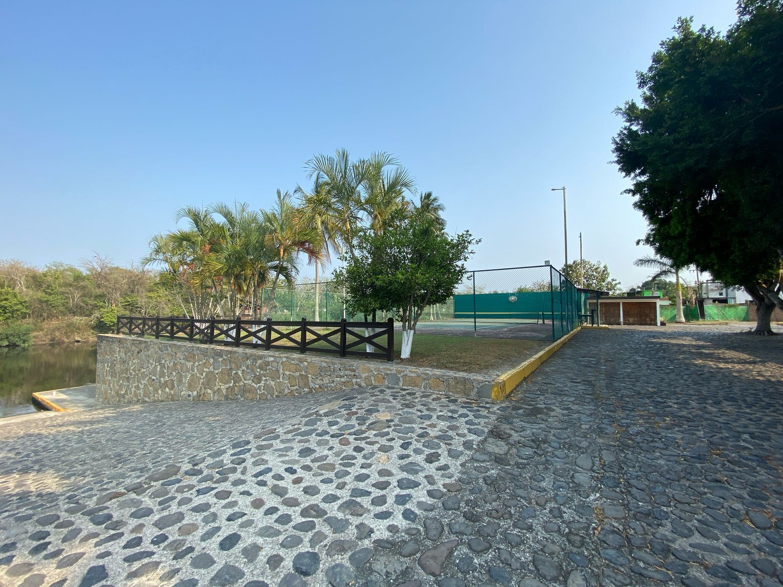 Un chemin pavé mène à une zone délimitée par une clôture, avec une étendue d’eau d’un côté.