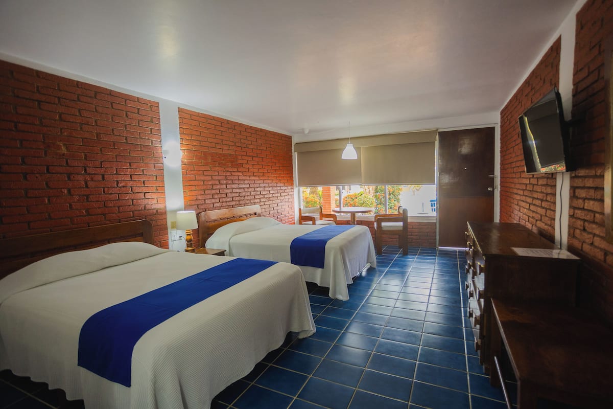 A hotel room with two beds, a TV, and a view of the outdoors.