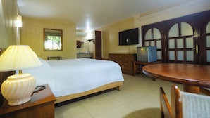 A hotel room with a bed, a wooden dresser, a television, and a dining table.