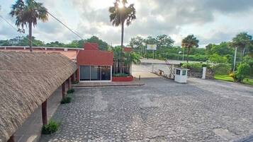 A courtyard with a cobblestone floor, a thatched-roof structure, and a red building with glass windows.