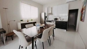 A modern kitchen with white cabinets, a dining table with four chairs, and a window with curtains.
